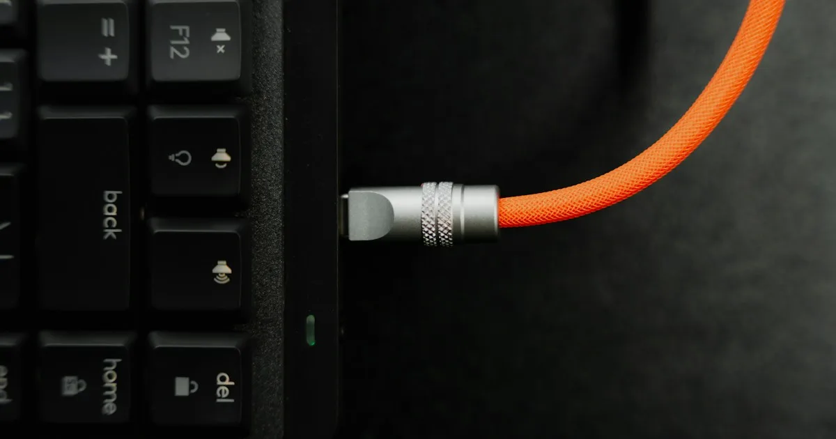 Close-up of a USB charging cable plugged into the rear edge of a keyboard, the clearance area a rear riser affects